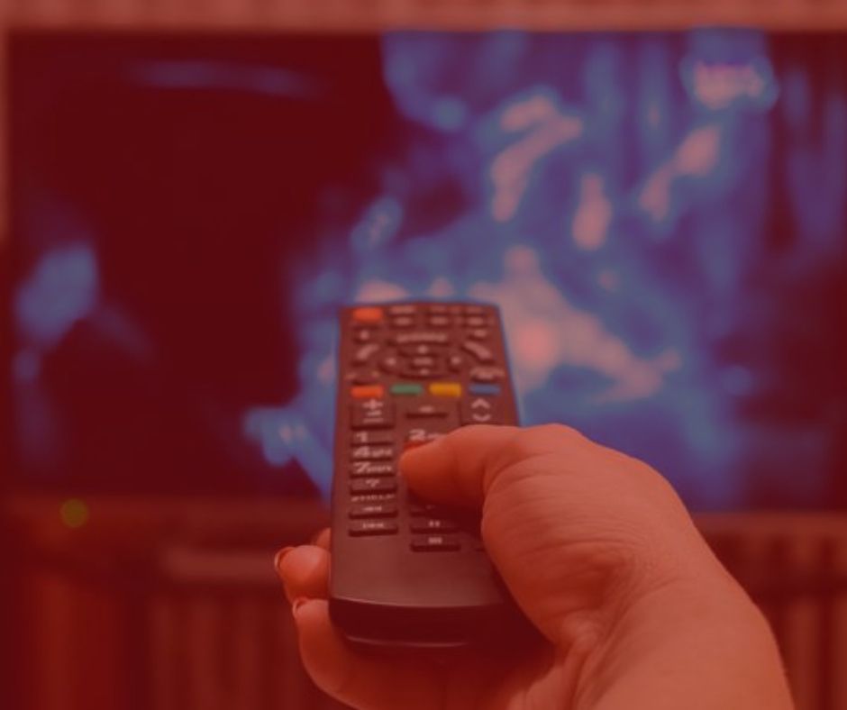 imagem simbolizando o direito do consumidor, uma pessoa segurando um controle remoto apontado para uma televisão, que esta com uma imagem no tom azul. Imagem com fundo vermelho.
