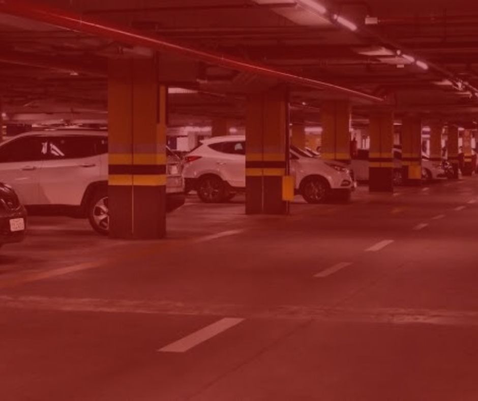imagem com fundo vermelho. Artigo: Responsabilidade dos estacionamentos por danos havidos a seus clientes. Na imagem, um estacionamento com as colunas nas cores amarelas e pretas, há carros estacionados nas cores prata, branco e preto. 