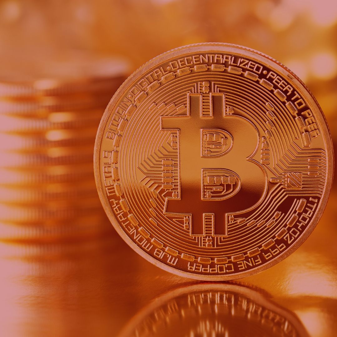 Notícia: Empresa gestora de bitcoins terá de indenizar e devolver dinheiro investido. Imagem com fundo vermelho, na foto uma moeda de bitcoins, moeda virtual. 
