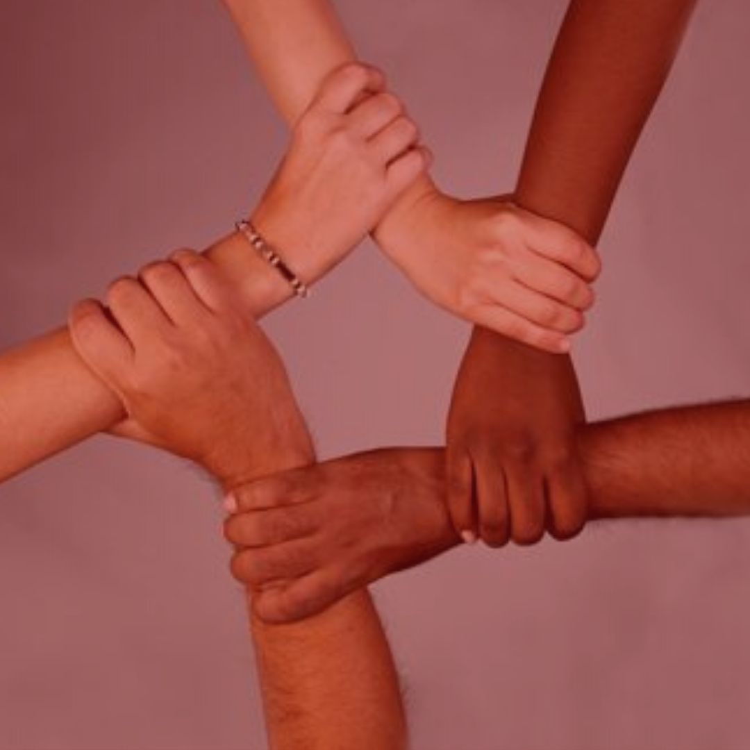 artigo: Injúria racial x racismo. Imagem com fundo vermelho, na foto, 4 braços dando mãos dadas.