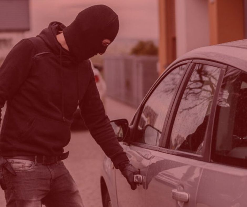 Notícia: TJ-SP condena supermercado a indenizar cliente por furto em estacionamento. Imagem com fundo vermelho. Um homem roubando um veículo estacionado, carro na cor prata, homem vestindo uma roupa preta com touca e luvas. 