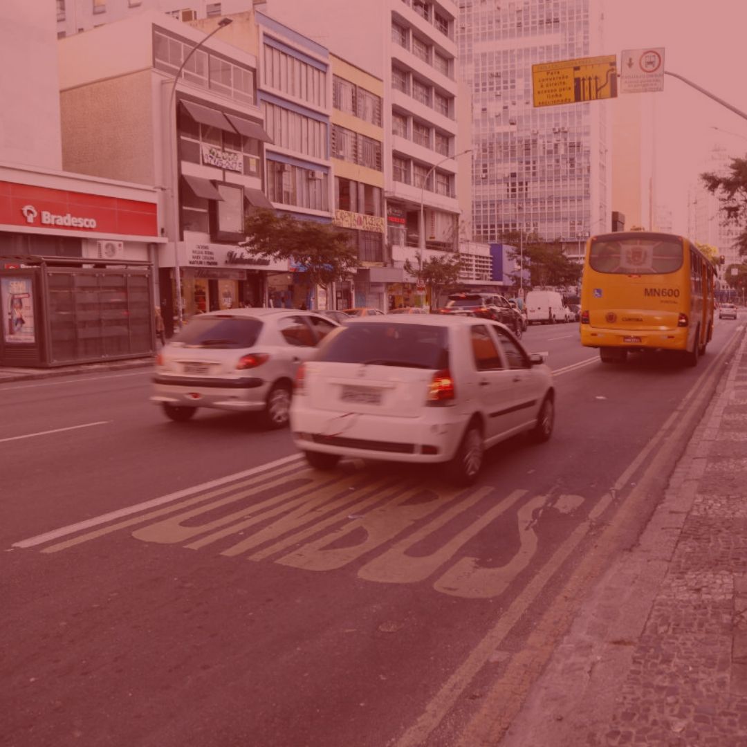 imagem com fundo vermelho. Notícia: Consumidor deve ficar atendo ao ressarcimento do Seguro DPVAT. Na foto, no centro de Curitiba, carros andando no transito. Cores na foto: branco, cinza, amarelo, vermelho, verde, azul, preto e amarelo. 