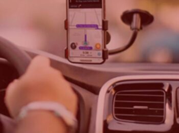 notícia: Uber fará corridas de graça para quem for doar sangue. #Pracegover: Na imagem o celular esta apoiado no parabrisa de um carro com o aplicativo Waze aberto. Cores na foto: preto, cinza, roxo, laranja e vermelho.