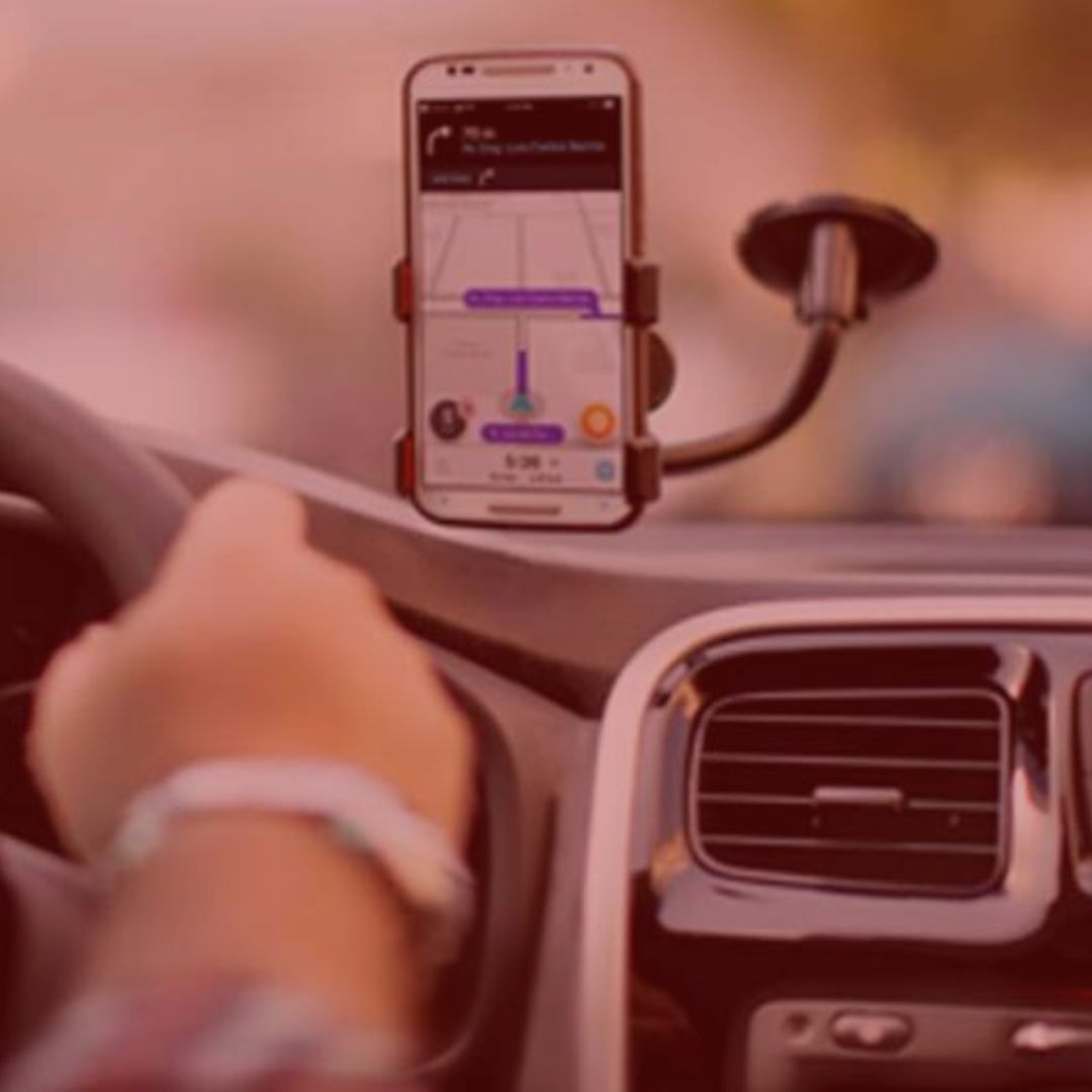 notícia: Uber fará corridas de graça para quem for doar sangue. #Pracegover: Na imagem o celular esta apoiado no parabrisa de um carro com o aplicativo Waze aberto. Cores na foto: preto, cinza, roxo, laranja e vermelho.