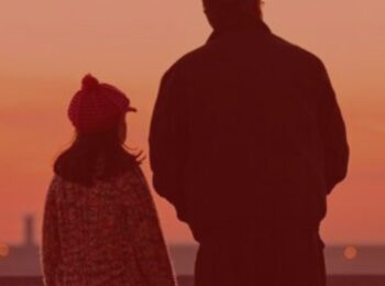 Notícia: Pai reverte decisão e poderá visitar filha durante a pandemia. #pratodosverem: pai e filha olhando a paisagem. Cores na foto: vermelho, laranja, preto .