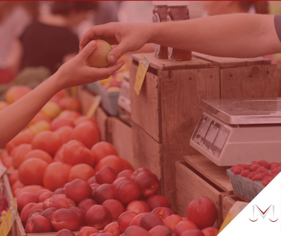 #pratodosverem: post: O vale-alimentação pode ser descontado do trabalhador ? - Na foto, uma pessoa realizando uma compra de frutas no mercado. Cores na imagem: vermelho, laranja, marrom, branco, preto e verde.