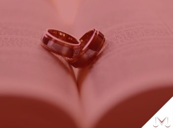 #pratodosverem: artigo: Os impedimentos matrimoniais. Descrição da imagem: Um livro com duas alianças em cima. Cores na foto: dourado, prata, branco, preto, cinza e vermelho.
