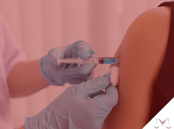 #pratodosverem: artigo: Demissão de não vacinados. Descrição da imagem: uma enfermeira está aplicando a vacina em outra pessoa. Cores na foto: azul, preto, branco, cinza e vermelho.