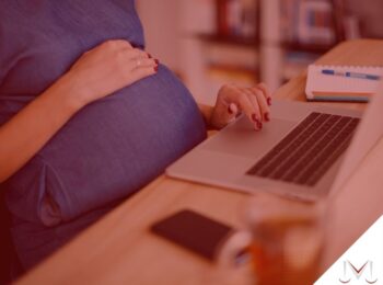 #pratodosverem: artigo: Gestantes podem voltar ao trabalho? Descrição da imagem: uma mulher grávida está digitando no seu notebook. Cores na foto: prata, preto, azul, vermelho, cinza, laranja e branco.
